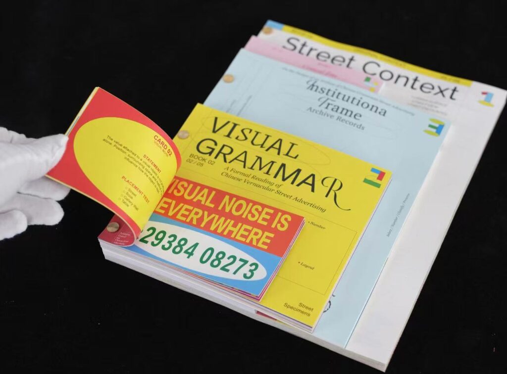A hand turns a page in a colourful set of printed publications, with Street Context and Visual Grammar visible underneath.
