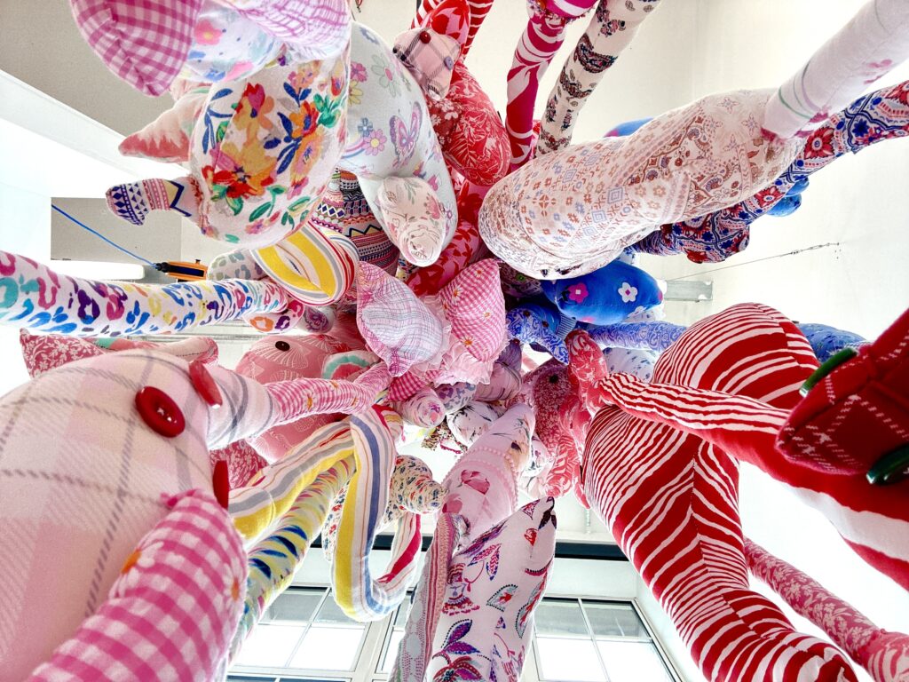 A side view of a suspended soft sculpture made from colourful second-hand textiles.