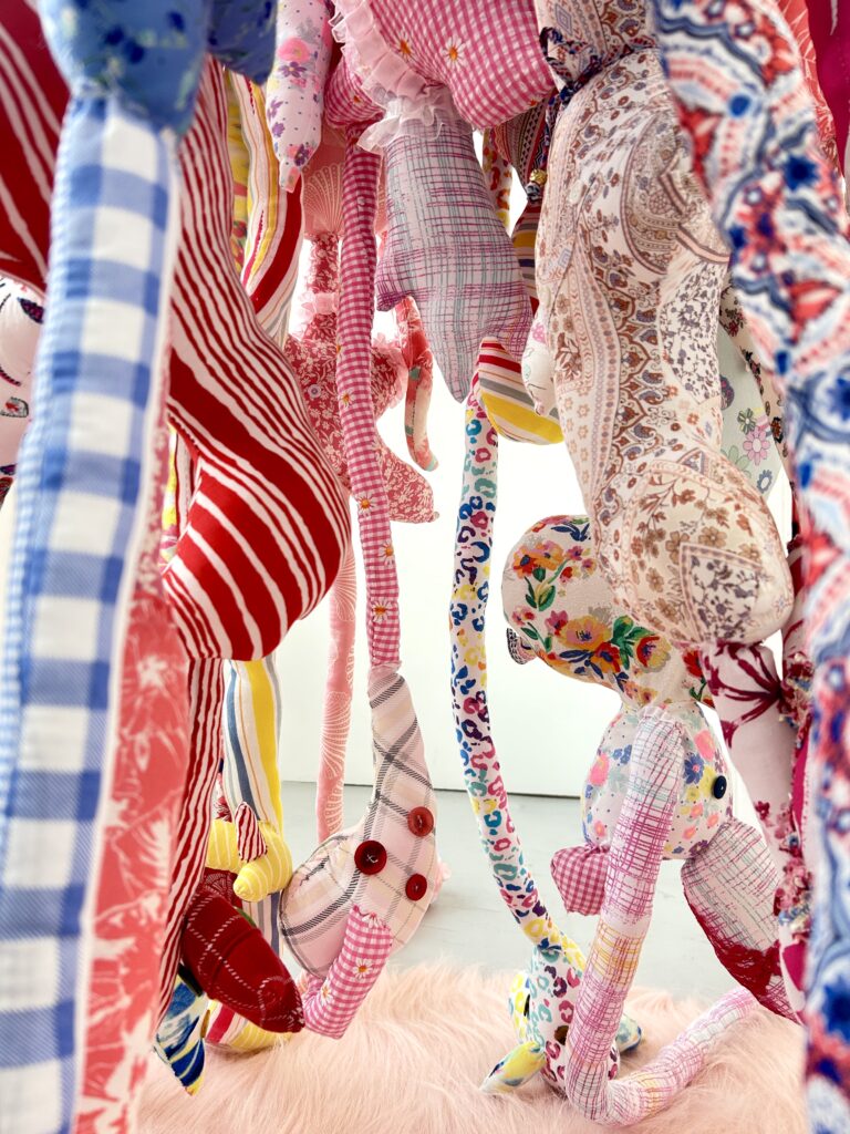 A side view of a suspended soft sculpture made from colourful second-hand textiles.