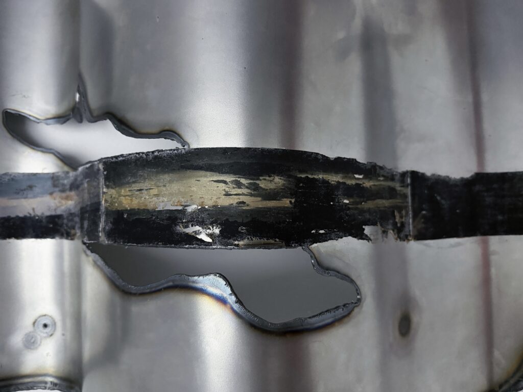 Close-up of a folded steel sheet showing a dark horizontal image transfer, plasma-cut openings and heat-darkened edges.