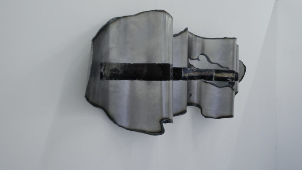 Side view of a folded wall-mounted steel sheet showing its curved profile, irregular cut edges and horizontal image transfer.