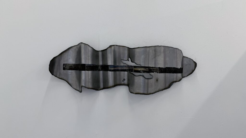 Front view of a wall-mounted folded steel sheet with an irregular outline, a dark horizontal image transfer, and small cut-out openings.