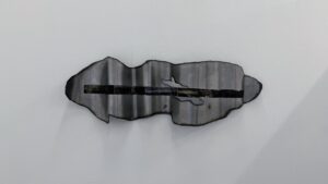 Front view of a wall-mounted folded steel sheet with an irregular outline, a dark horizontal image transfer, and small cut-out openings.