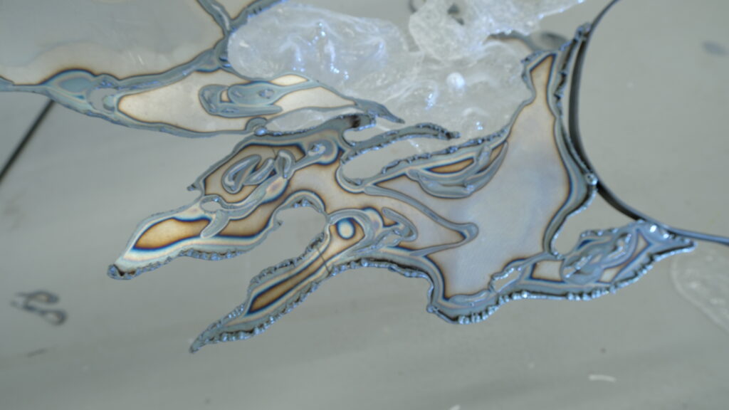 Close-up of plasma-cut steel showing heat marks, layered cut lines and irregular flowing edges.