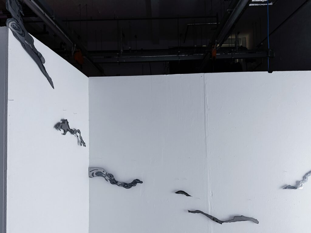 Wall-mounted plasma-cut steel fragments arranged across two white walls in an irregular flowing composition.