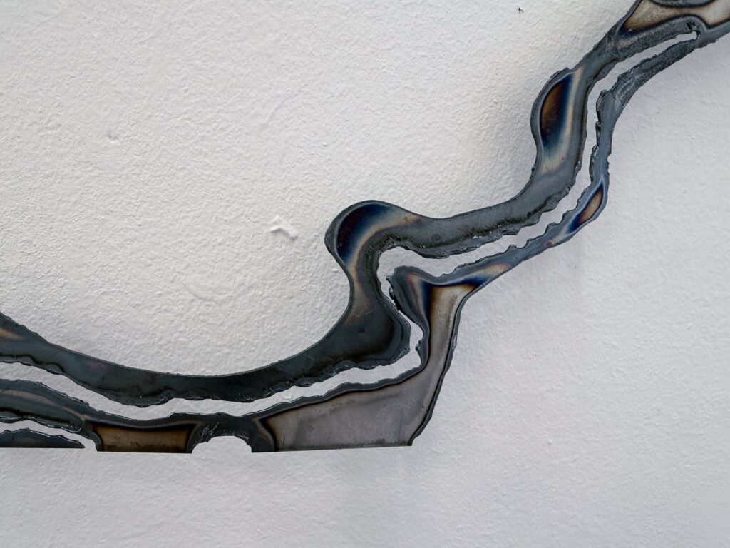 Close-up of plasma-cut steel showing darkened heat marks, irregular cut edges and curved linear forms.