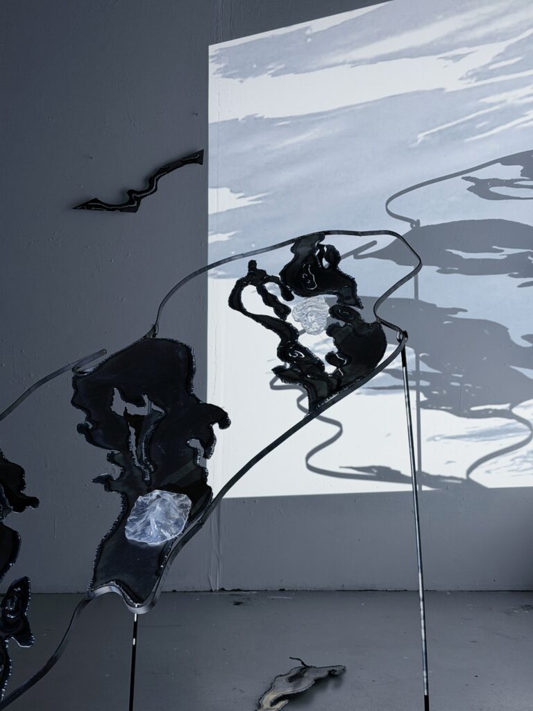 Close installation view of the raised steel structure and transparent resin elements in front of projected water imagery.