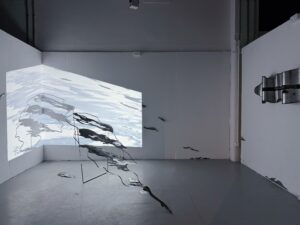 Wide installation view showing a steel sculpture extending across the floor, projected water imagery on the walls, and wall-mounted steel elements.