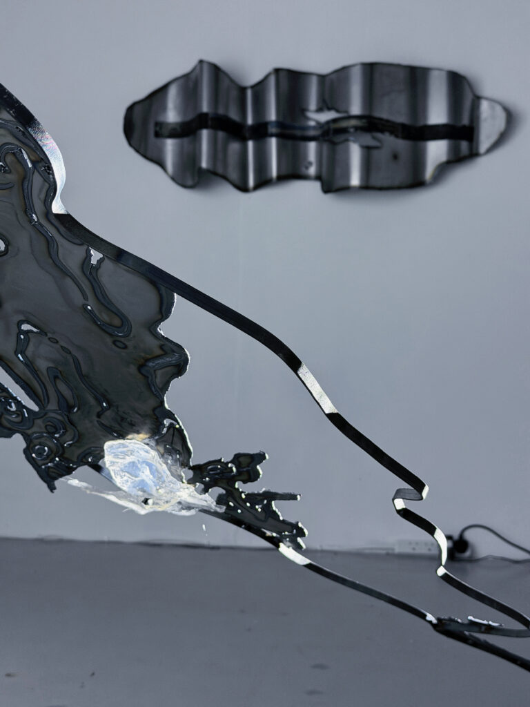Close-up of the curved steel structure and transparent resin, with a reflective wall-mounted steel work visible in the background.