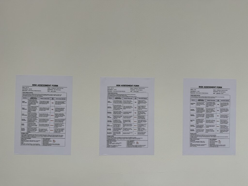 Three fictional risk assessment forms for Li Che, Jiaxi Kim and Chen Qi displayed on a gallery wall.