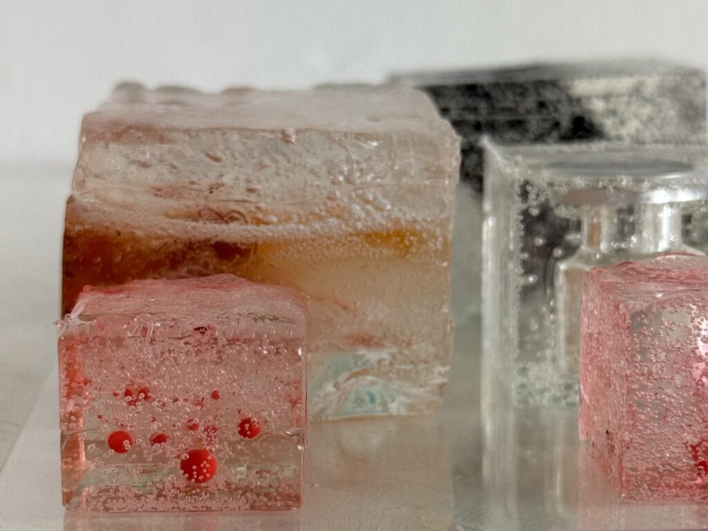 Close-up of translucent resin blocks containing medical and personal materials in pale pink, red and amber tones.