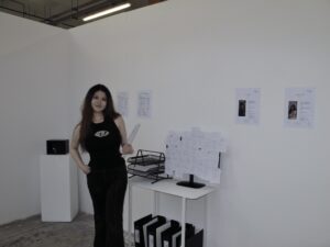 Mingyu Li standing within the LMy Artist Agency office installation, surrounded by fictional artist archives and institutional materials.