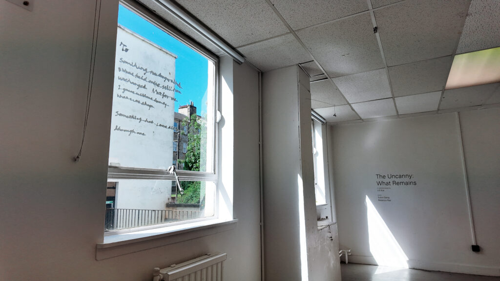 Installation view of The Uncanny: What Remains, showing wall text, translucent curtains and daylight entering the exhibition space