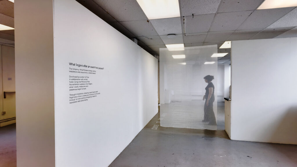 Installation view of The Uncanny: What Remains, showing wall text and sheer curtains in the exhibition space
