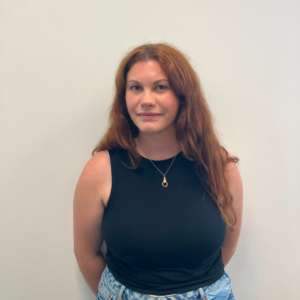 Image of a woman with ginger hair and a black t shirt looking at the camera
