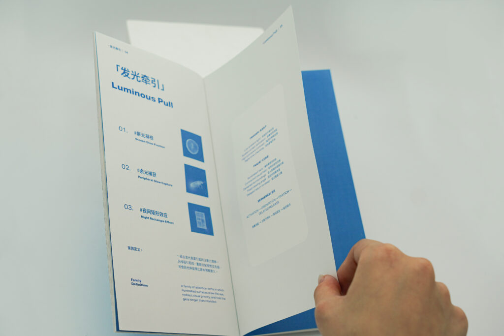 An open publication showing the Luminous Pull family page while a hand turns a translucent sheet, revealing blue printed information and a dark blue insert beneath.