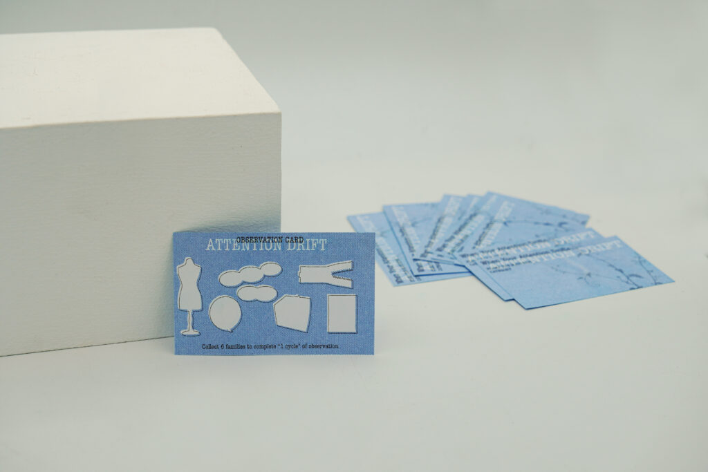 A small blue Attention Drift Observation Card stands beside a white display block, with several additional cards arranged behind it. Six empty shapes on the card correspond to the project's six attention-drift families.