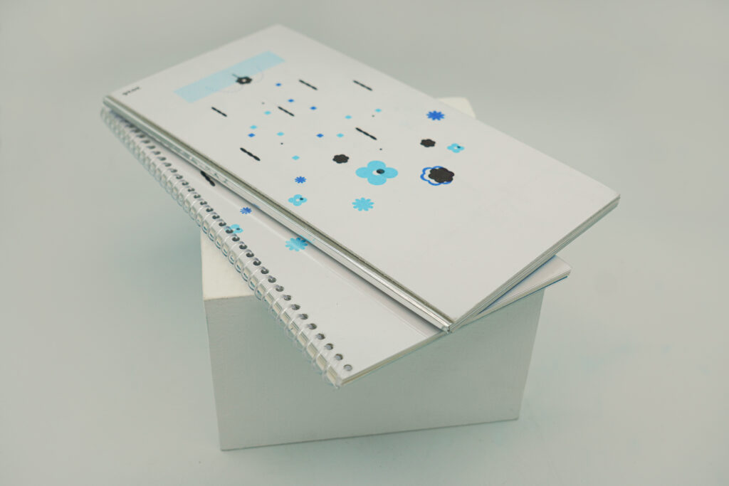 Two physical editions of An Index of Ways Attention Drifts Away are displayed together on a white block, showing the back covers of both publications.