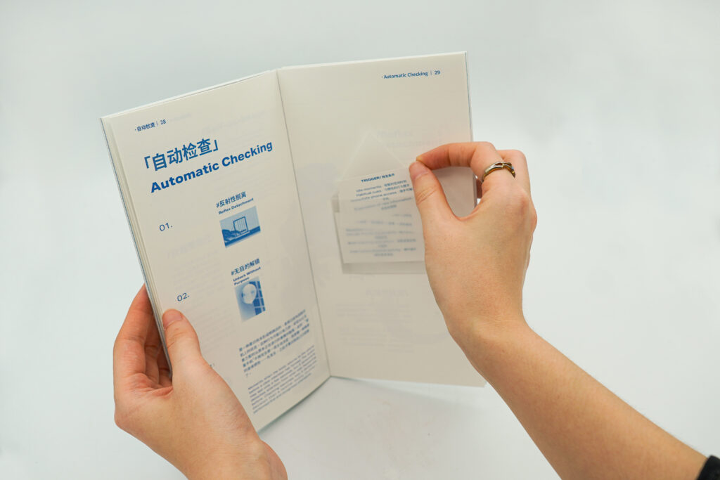Two hands hold an open publication showing the Automatic Checking family. A transparent folded paper element containing printed trigger information is being lifted from the right page.