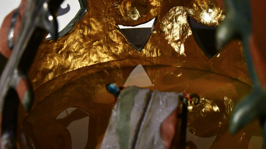 a tongue emerges from the centre of the interior gold-gilded space of a rounded form with circular and triangular shapes in the walls, water covers the bottom.
