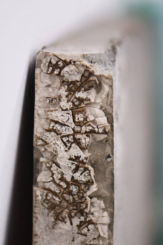 a cracked grey surface of a concrete cast book leaning against a white-painted wall